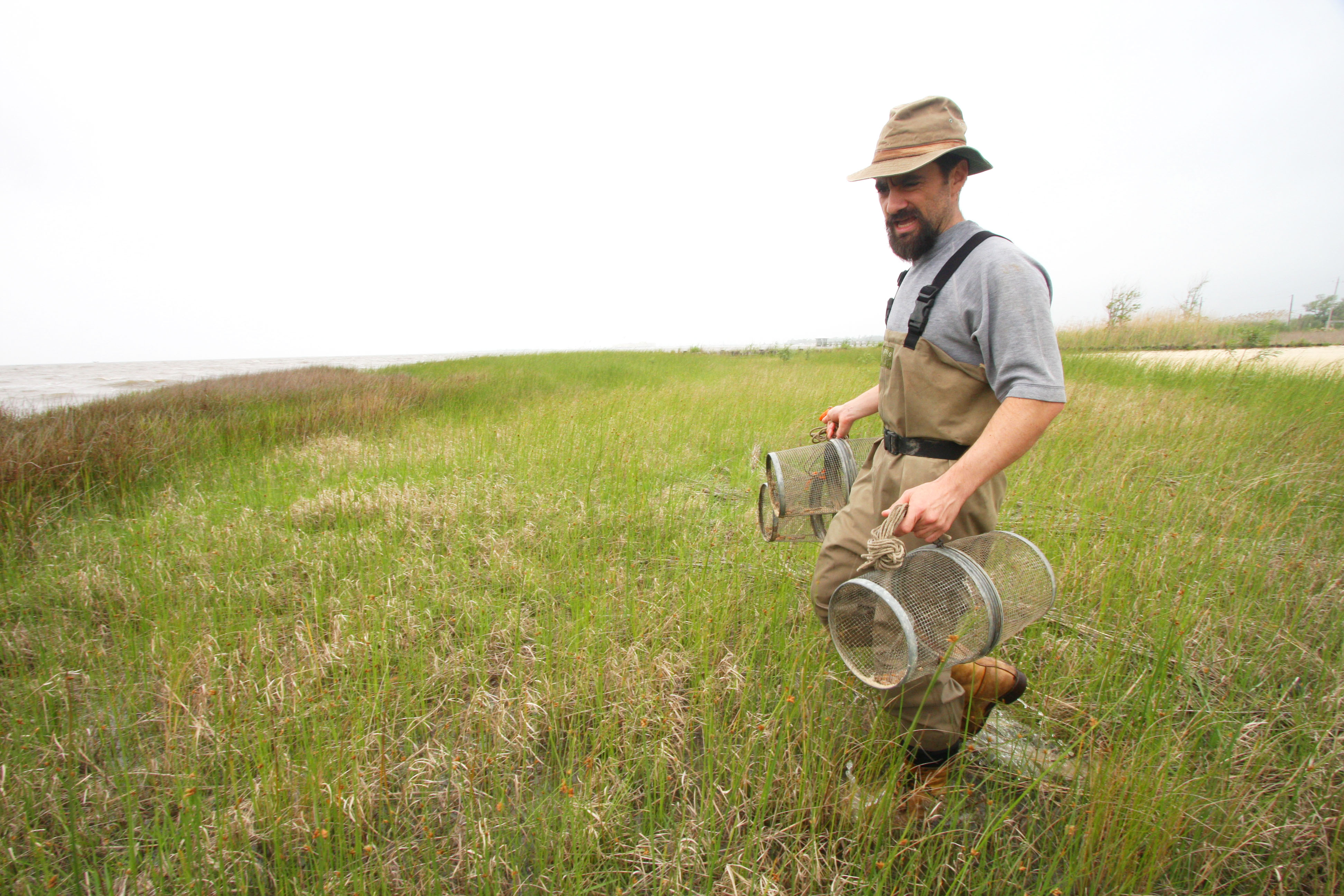 A man holds two minnow traps while wearing waders.