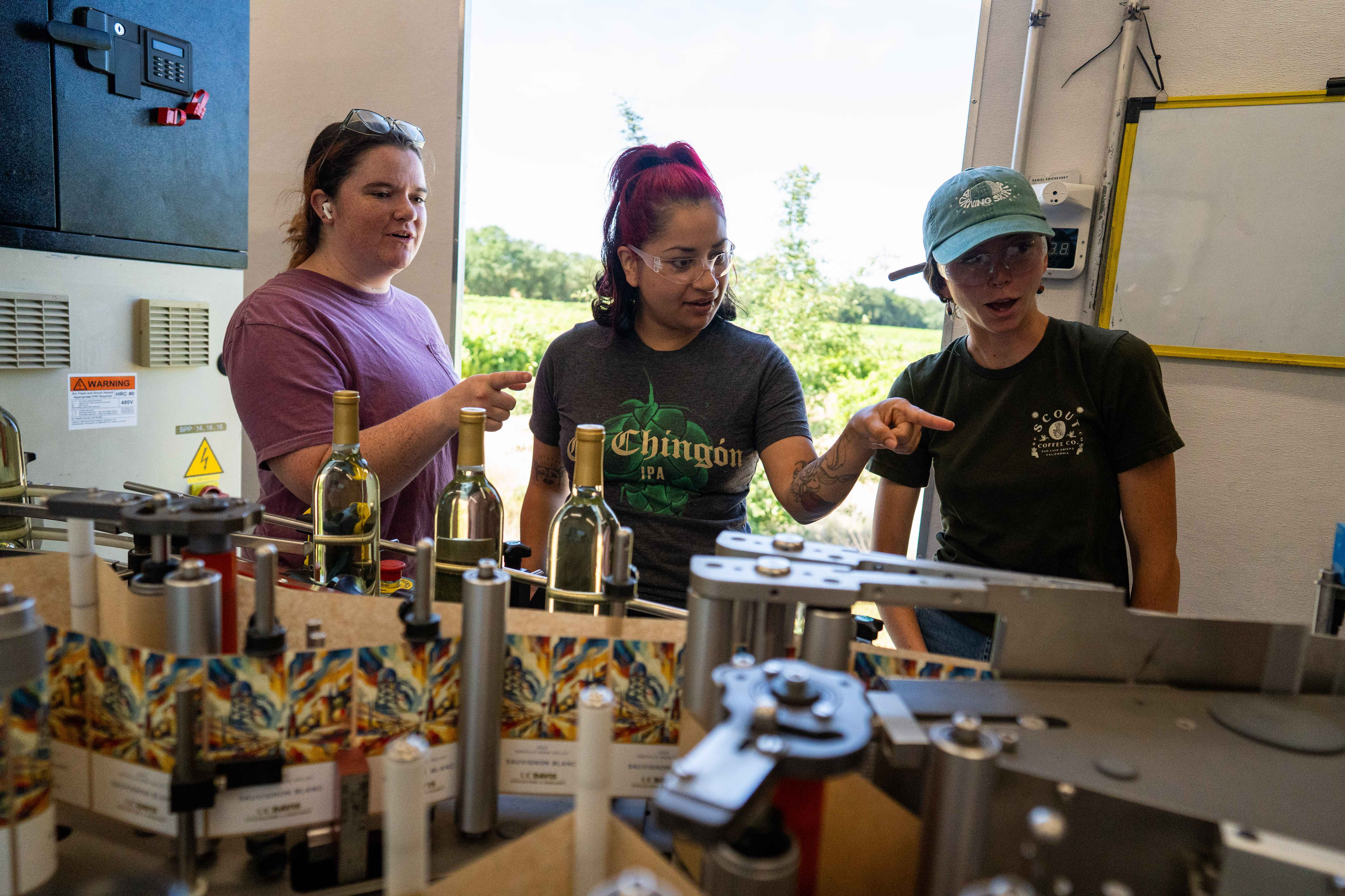 Three students at a bottling line, one pointing to a bottle