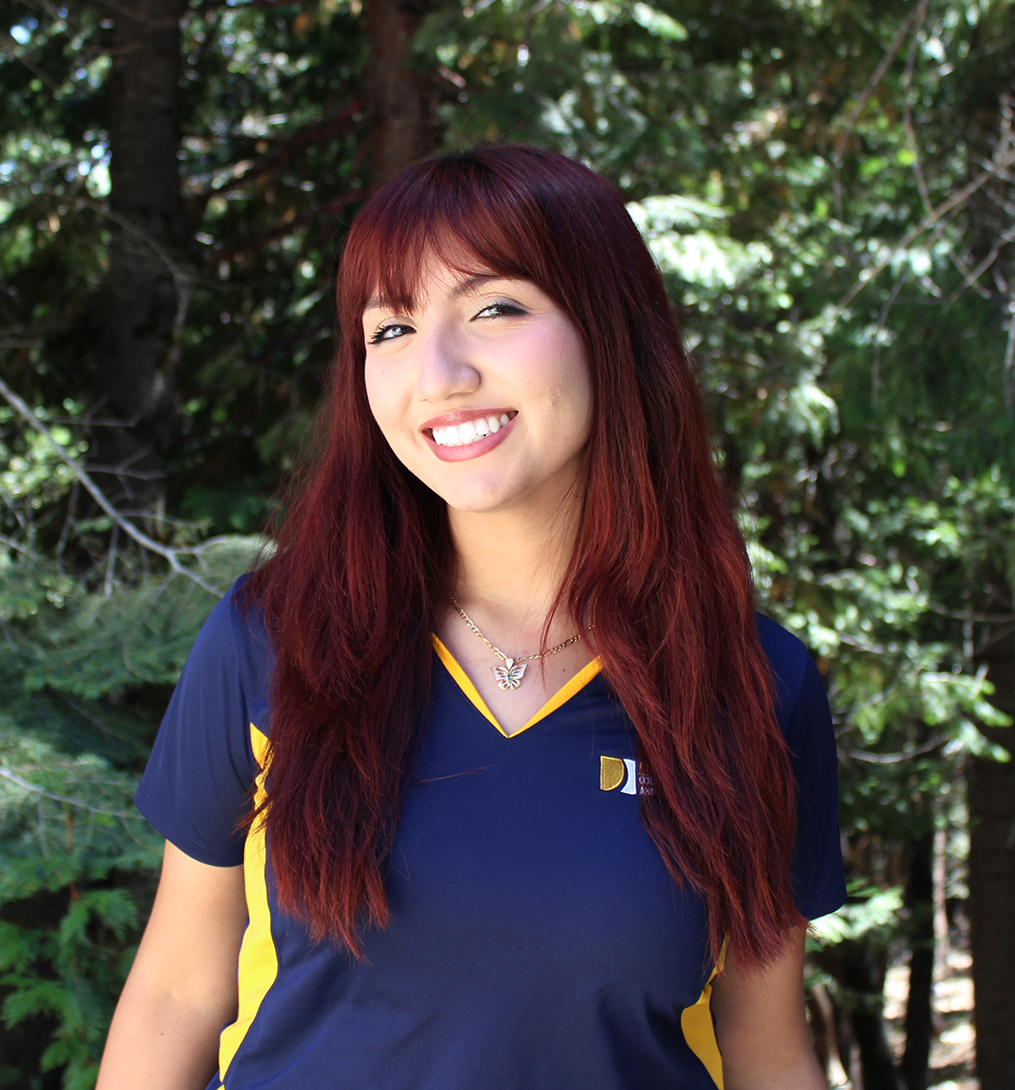 Smiling young woman with long red hair in navy shirt standing outdoors among trees