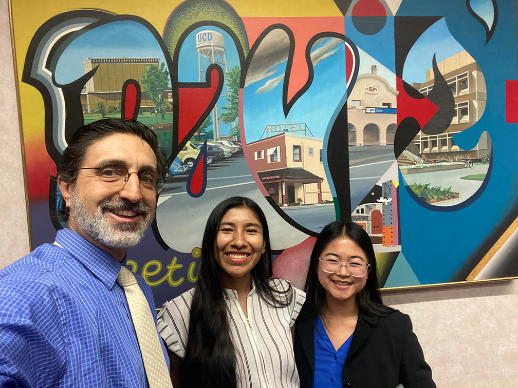 A man takes a selfie with with two women in front of a sign that says Davis.