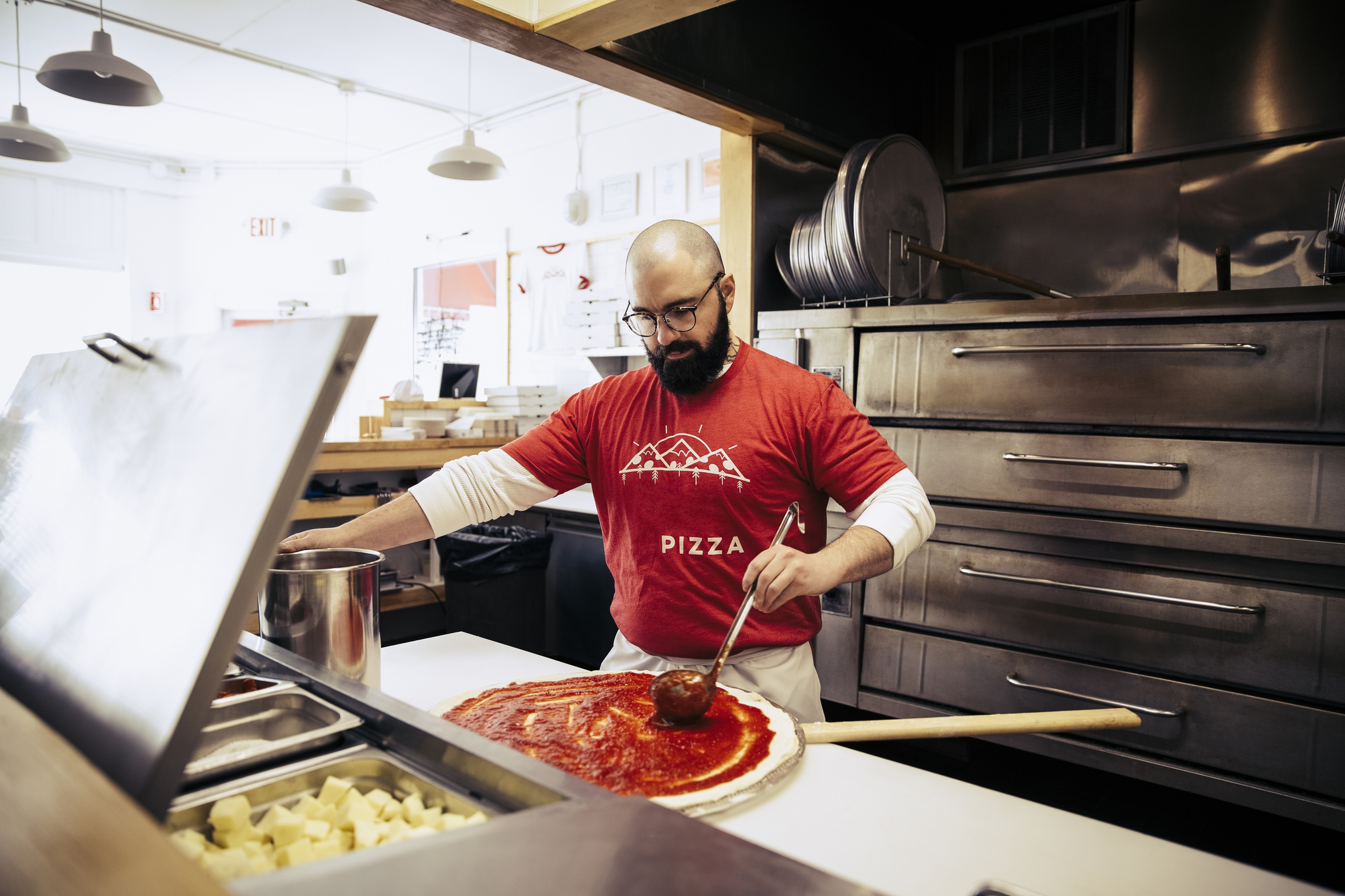 A man puts marinara sauce on a pizza before putting the food into an oven.