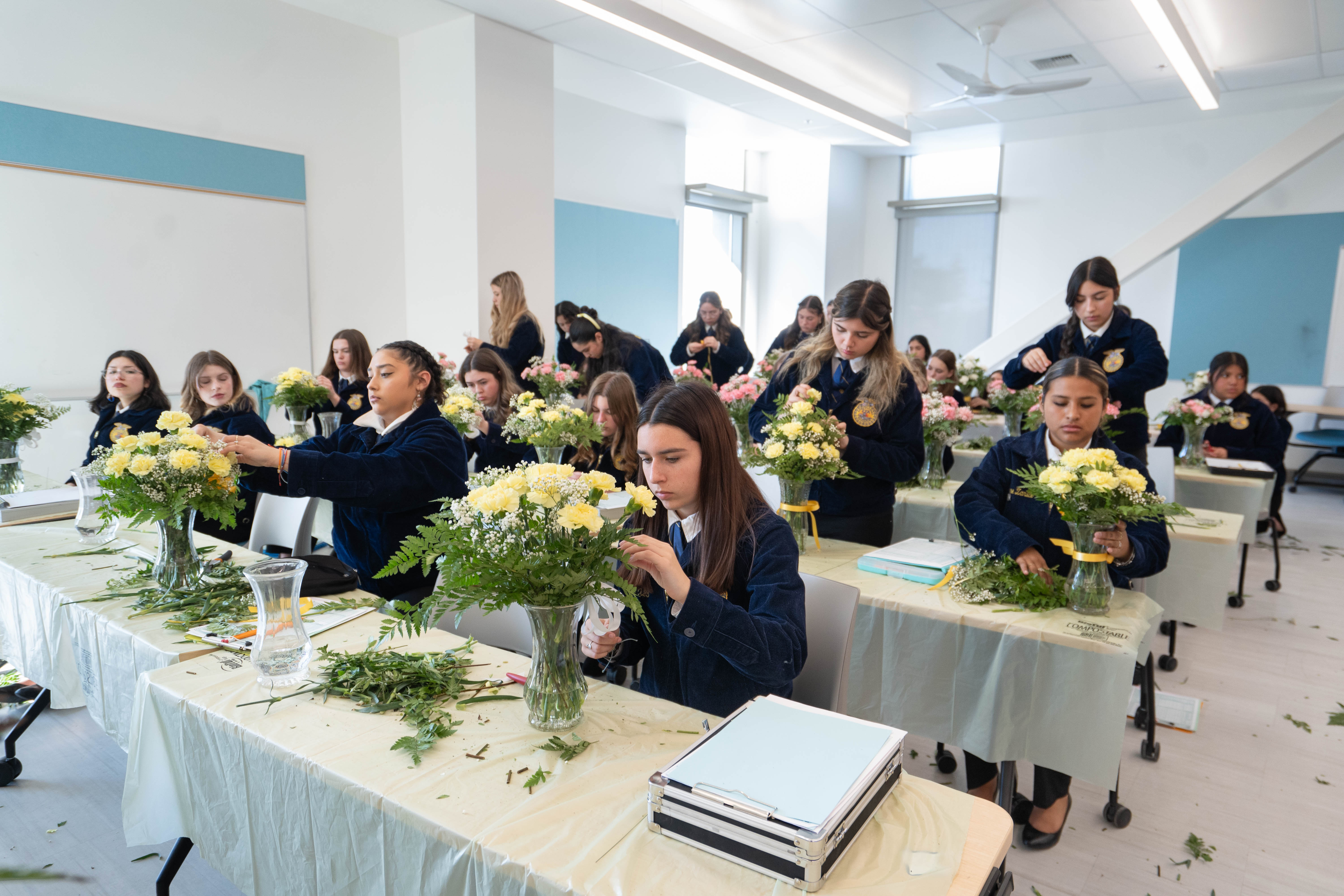Students crafting floral arrangements in a bright classroom, focused on their work.