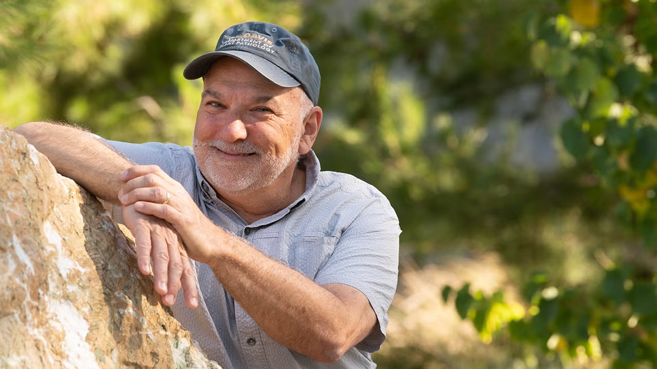 Smiling older man in cap leaning on a rock in a sunlit outdoor photo