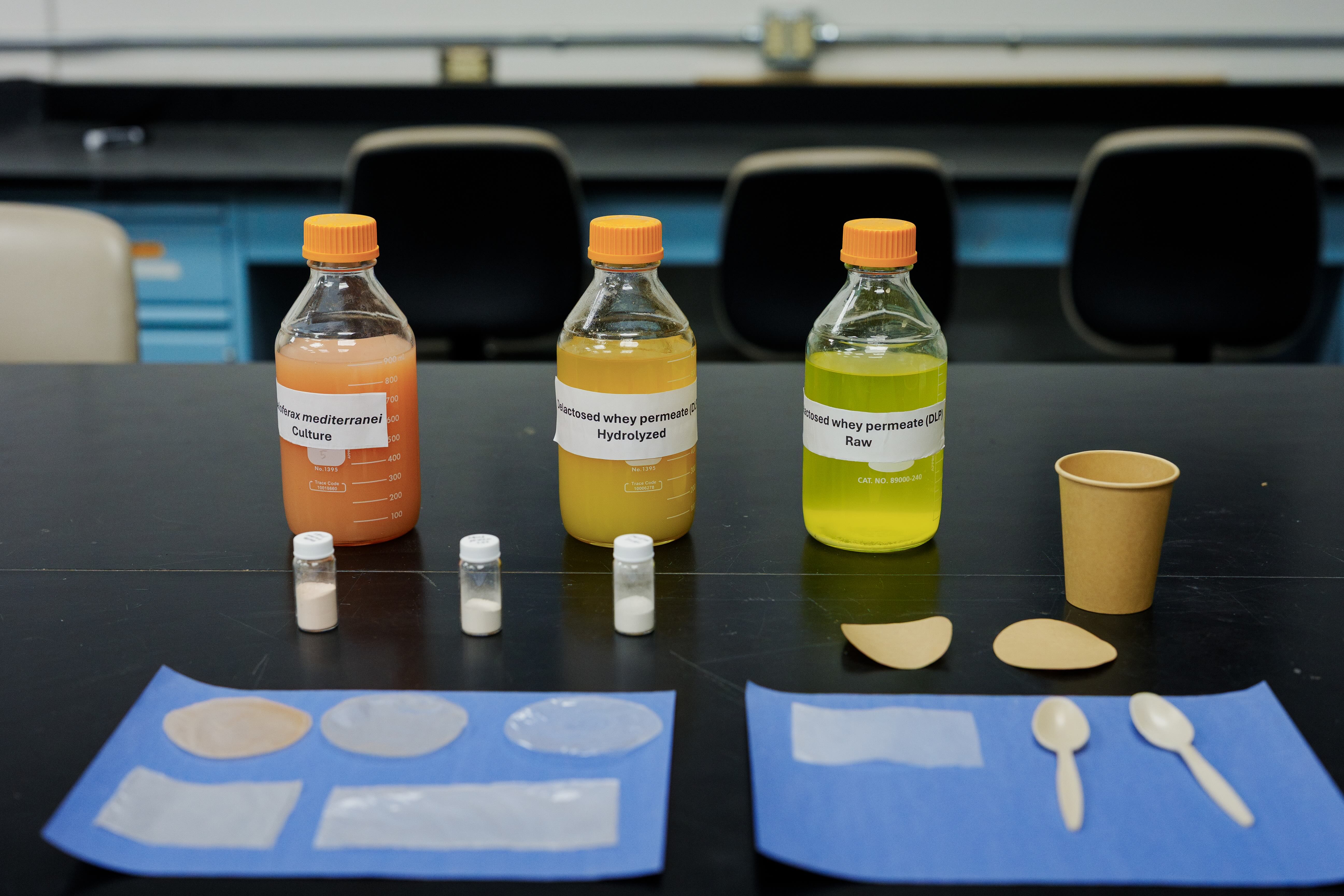 Lab table with three bottled liquids, small sample vials, paper cup and wooden spoons