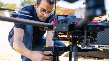 A person is handling the drone, possibly preparing it for flight in an outdoor setting