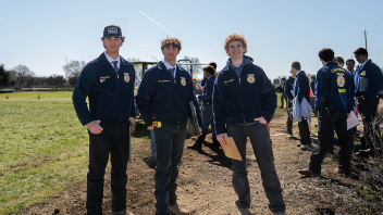 Three people in blue jackets stand out in a field.