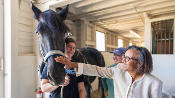 A woman pets a horse's nose while a student holds the horse's reins.