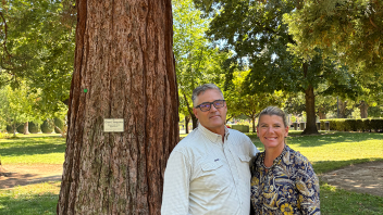 Two people stand together under a large tree.