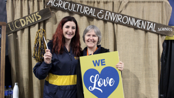 Co Hawes holds up a pom pom while hugging Sue Ebeler as she holds up a "We Love UC Davis" sign.