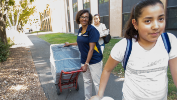 A person pulls a refrigerator using a cart behind another person.