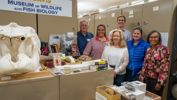 The group stands in an aisle in the museum with tortoise shells and large mammal skulls used for teaching in the foreground.