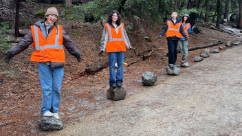 Students stand on top of rocks while outside the forest.