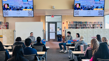 People seated at tables looking at people presenting information.