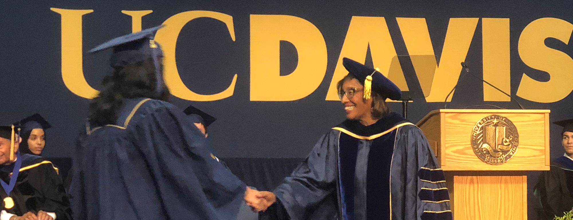 Helene Dillard shakes hands with a college graduate.