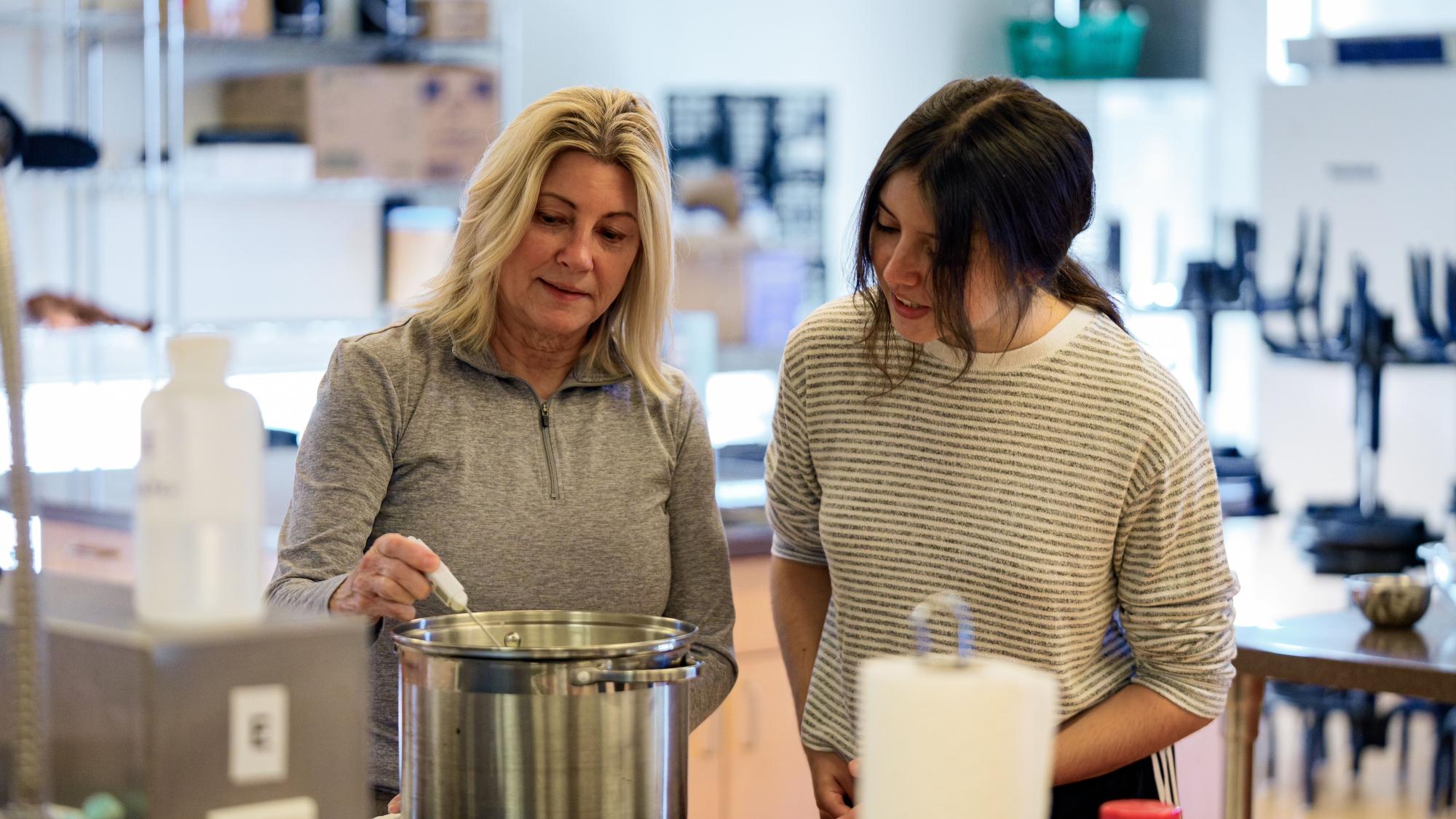 Two women smiling in a modern kitchen, one stirring a large pot