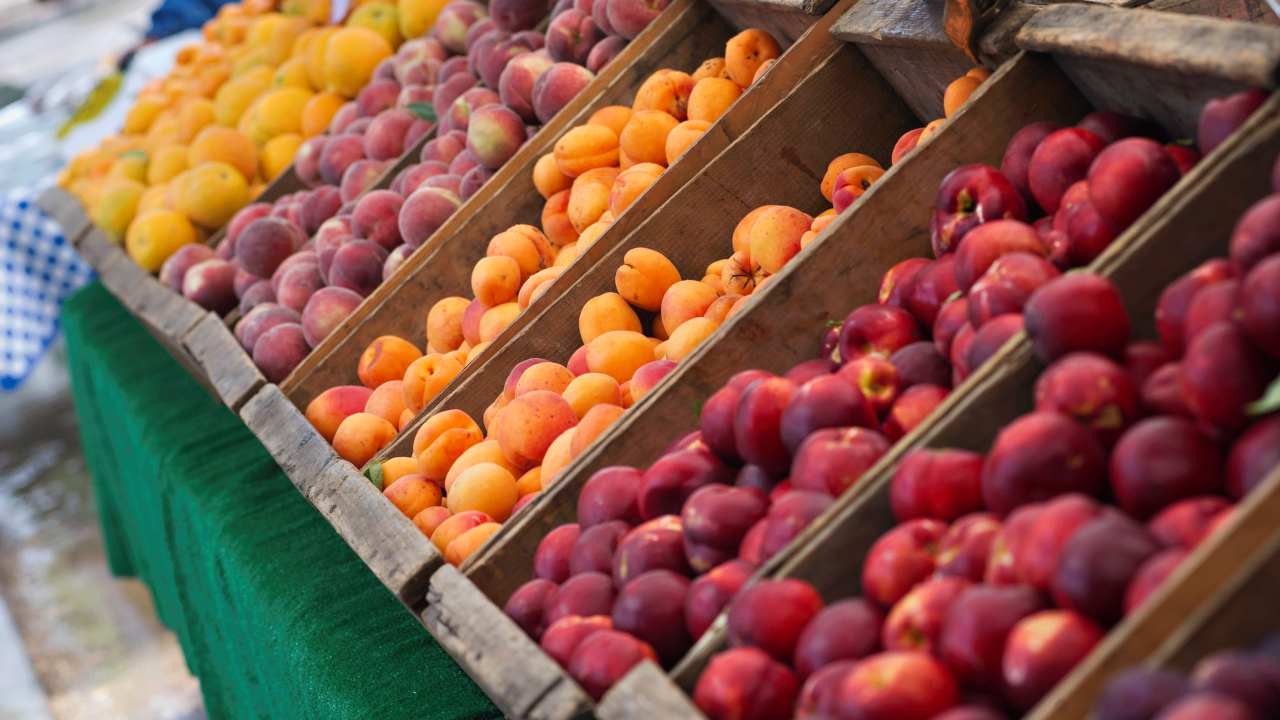 A row of stone fruit in wooden boxes at a Farmers market.