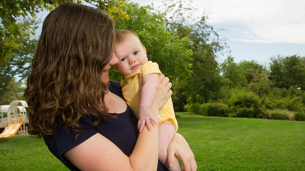 A woman stands outside holding a newborn baby.