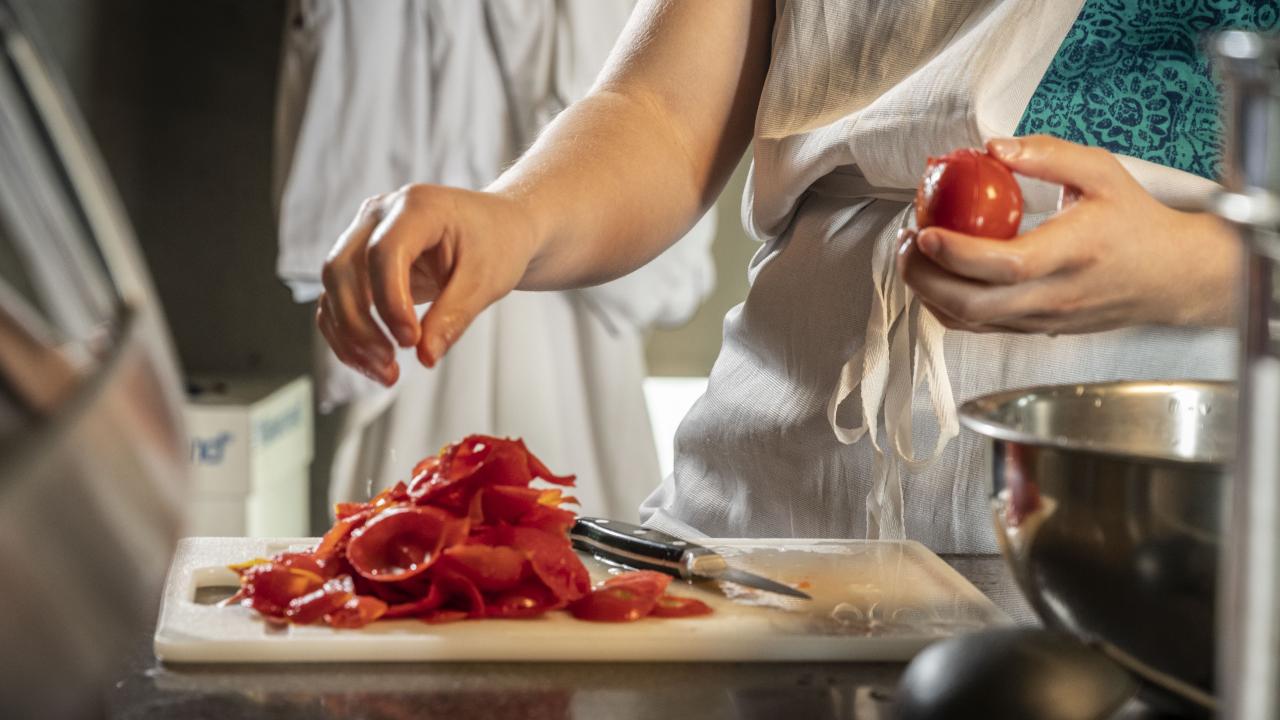 Hands preparing tomatoes to make canned tomato sauce.