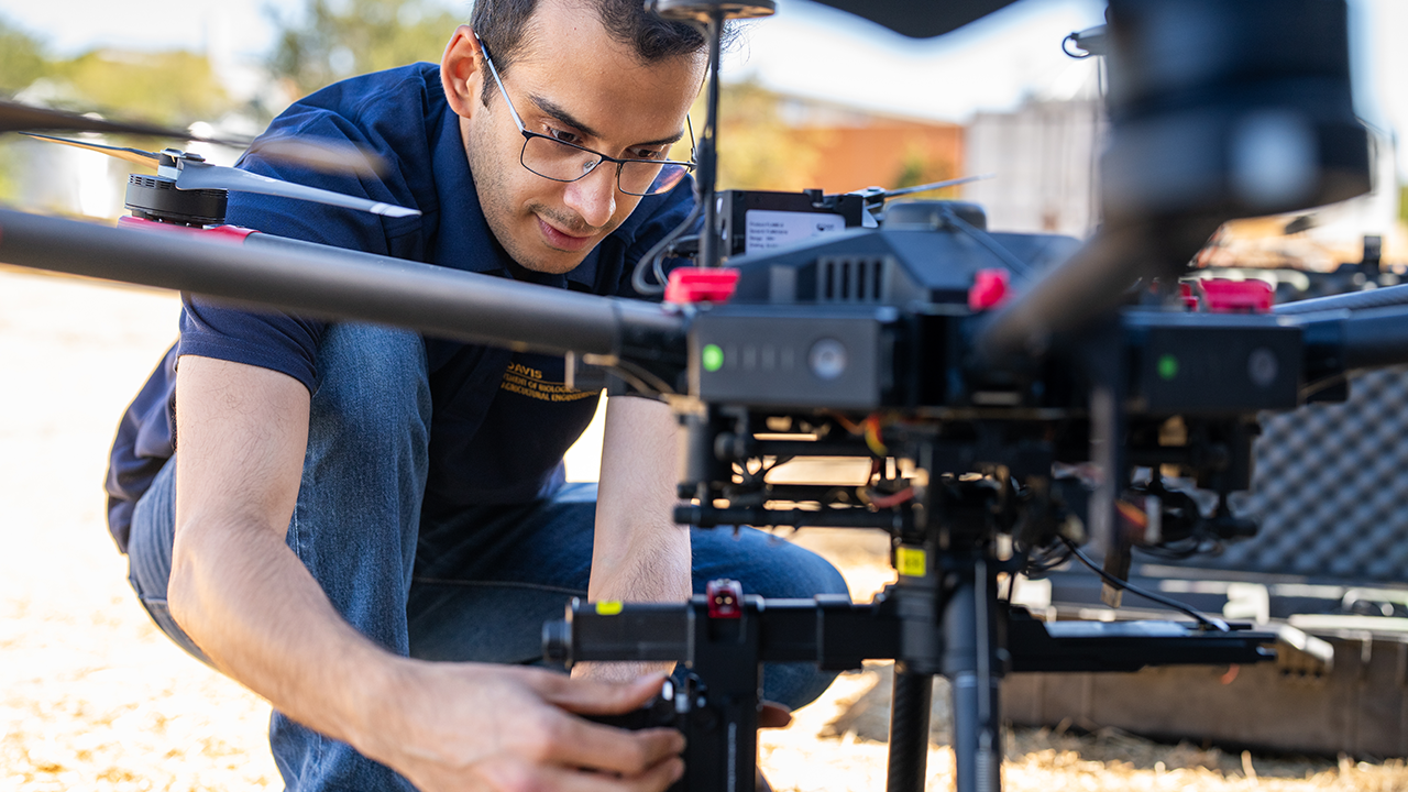 A person is handling the drone, possibly preparing it for flight in an outdoor setting