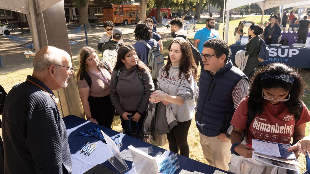Three undergraduates in "Becoming a Latino Scientist," from the left Kaitlyn Menjivar-Esquivel, Itzel Gonzalez and Peyton Apruzzese, learn about opportunities at the Graduate and Law School Fair on the Quad Oct. 23 for an assignment given by instructor Luis Carvajal-Carmona, (center), a professor of biochemistry and molecular medicine who oversees campuswide Avanza HSI initiatives as associate vice chancellor for academic diversity in Diversity, Equity and Inclusion.