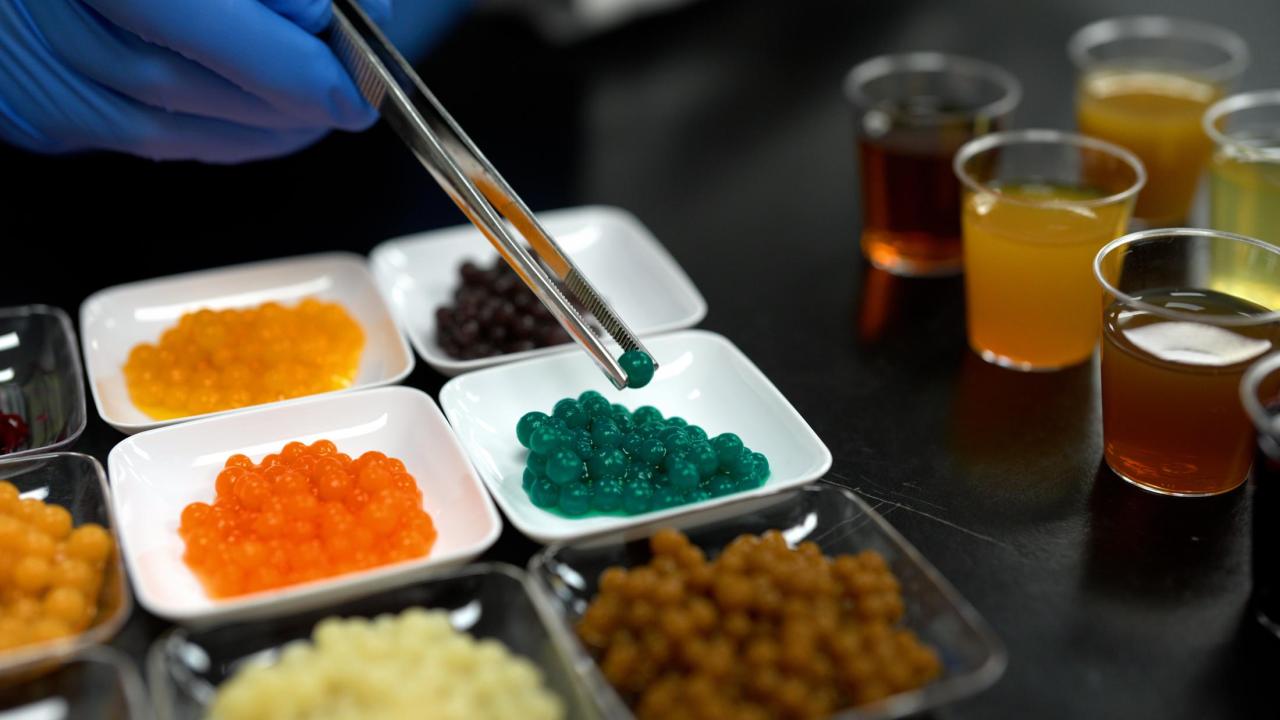 Tweezers lift a boba pellet from a tray of green boba.