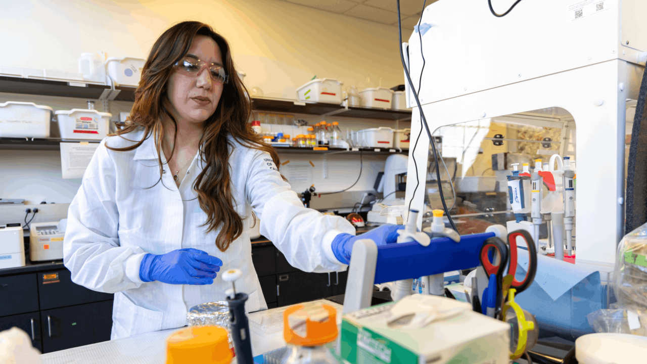 A scientist in a lab coat and gloves works with equipment and lab materials.