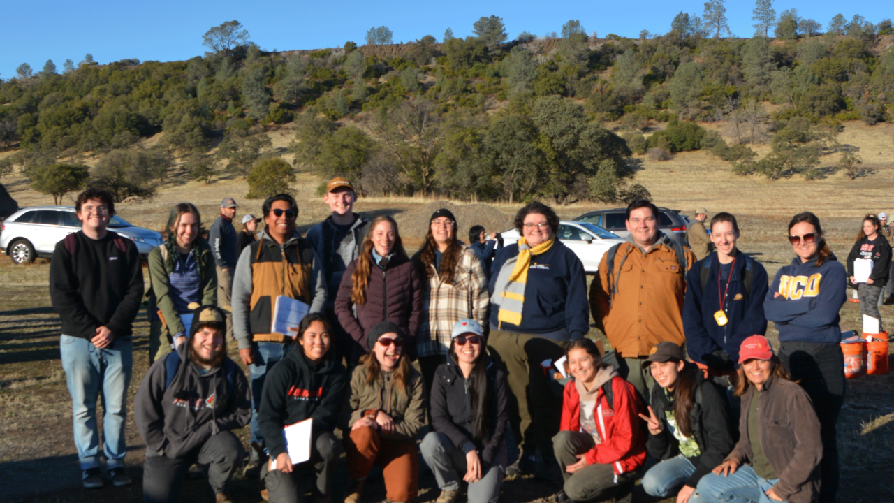 A group of people stand together posing for a group shot outside.