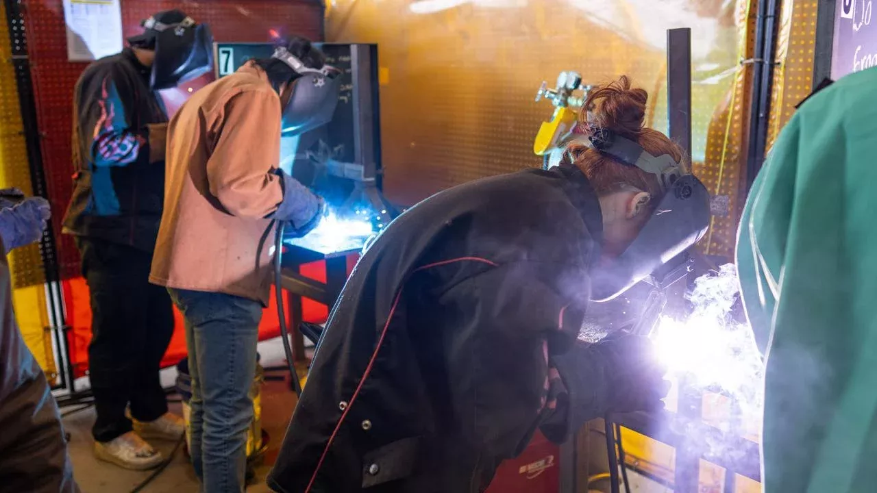 Bright sparks are visible from the welding process, indicating that metal work is being performed. The individuals are wearing protective gear, including helmets with visors and gloves, which is essential for safety during welding.