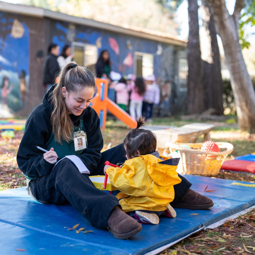 A student working with a toddler in the playground outside the Early Childhood Learning Lab.