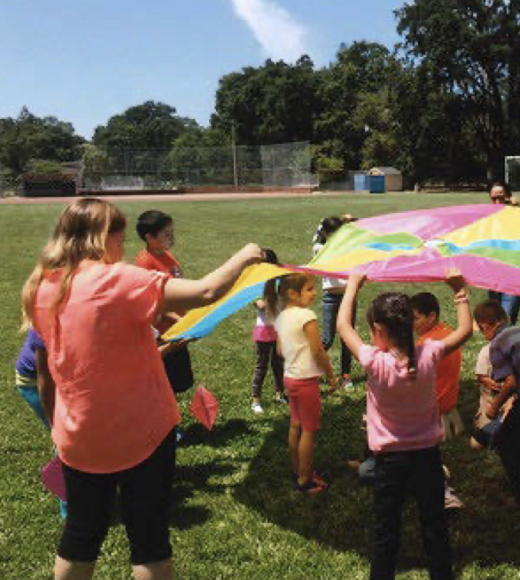 Kids playing underneath a colorful parachute.