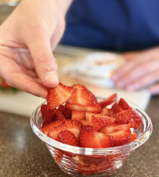 student places sliced strawberries into a glass bowl