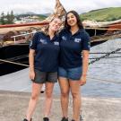 Two women standing together on a dock next to a boat.