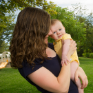 A woman stands outside holding a newborn baby.