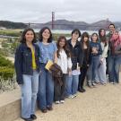 group of people including college students pose outside on a San Francisco overlook with Golden Gate Bridge behind them.