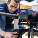 A person is handling the drone, possibly preparing it for flight in an outdoor setting