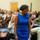 A woman stands and smiles as people around her applaud her.