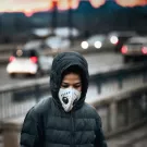 The photo shows a person standing on a bridge, looking out at a road with cars moving below. 