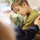 Young boy hugging a pillow on a sofa as an adult comforts him