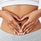 Hands forming a heart shape over a bare abdomen.