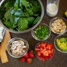 A kitchen counter with an array of ingredients including spinach, strawberries, avocado, almonds, cheese and mushrooms to prepare a salad.