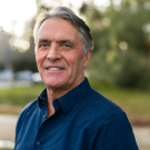 John Eadie wearing a blue button down shirt stands outside on the UC Davis campus.