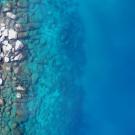 Aerial photo of rocky shoreline with turquoise shallow water fading to deep blue sea