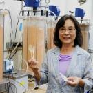 Smiling researcher in lab coat holding a vial beside scientific equipment.