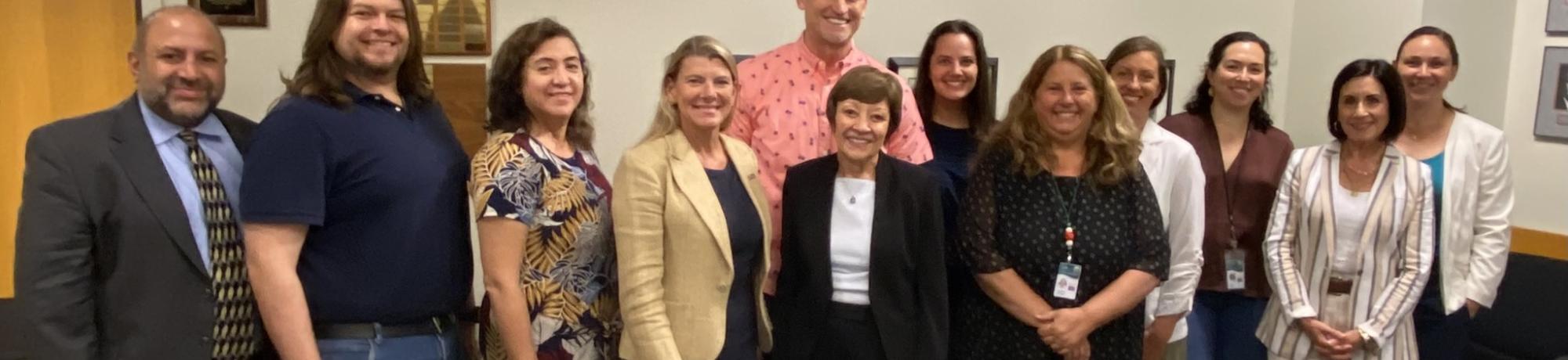 Group of people stand together smiling while wearing business attire.