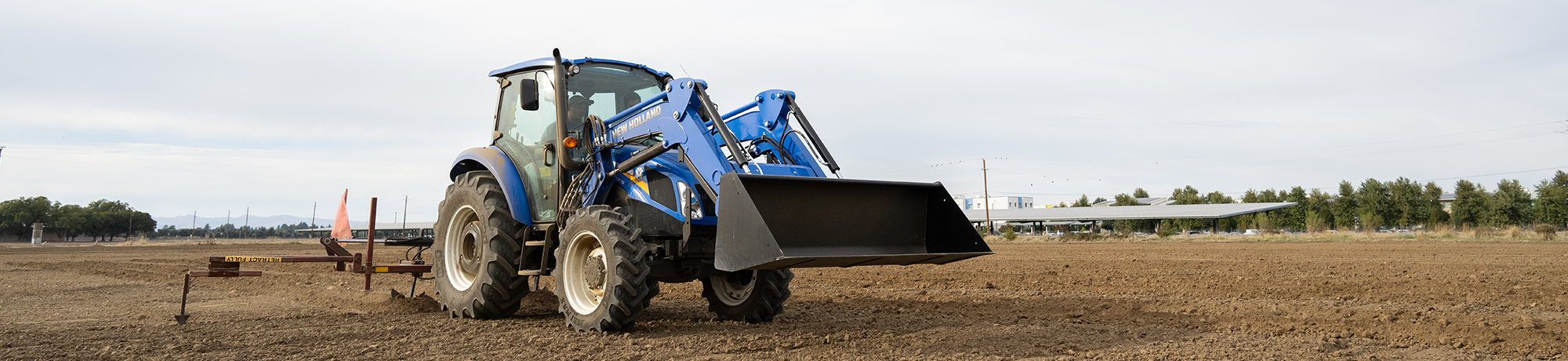 A blue and gray tractor with a front loader attachment, parked on cultivated farmland.