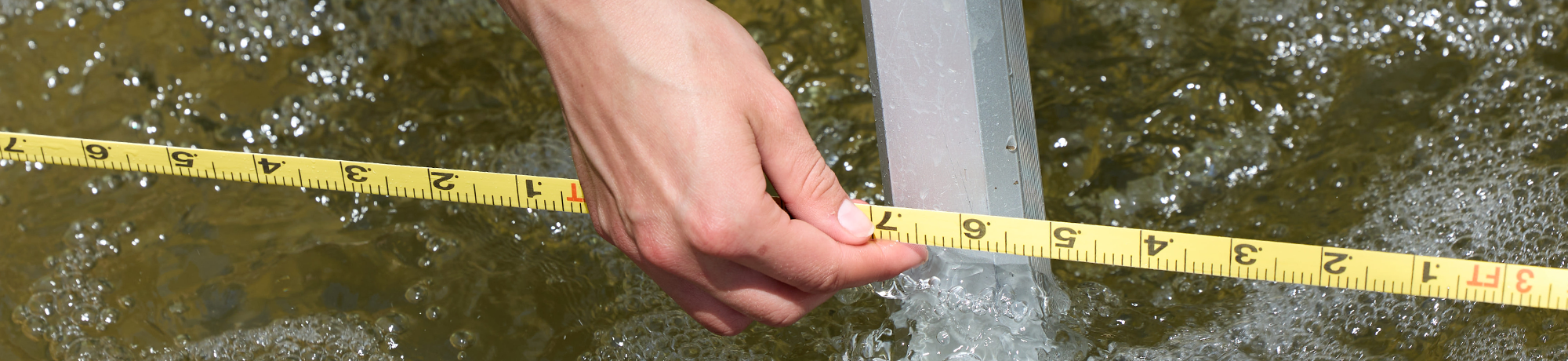 A measuring tape is held above a body of running water.