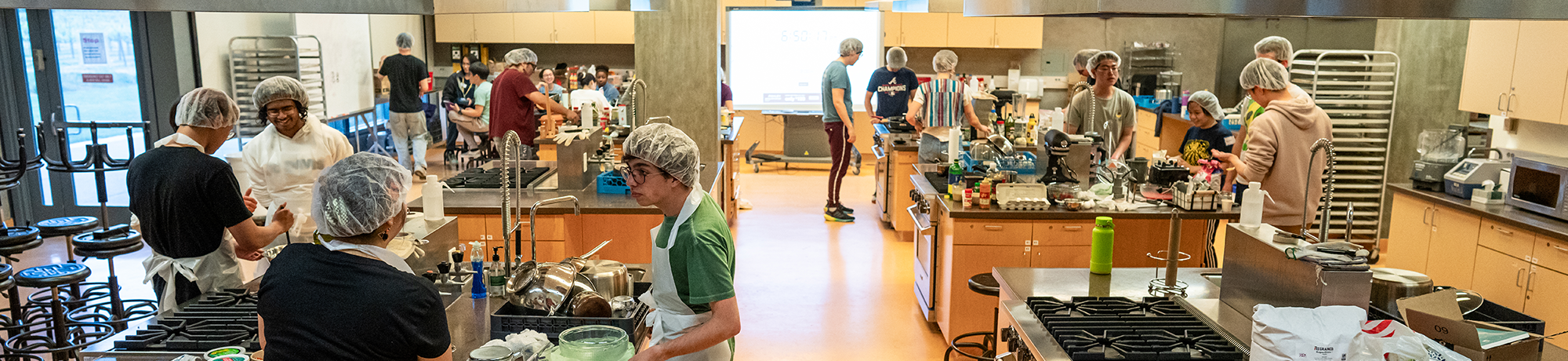 Groups of people at different cooking stations in a classroom lab.